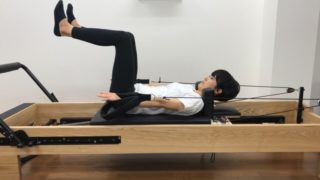 ピラティスリフォーマーでカールアップをする女性