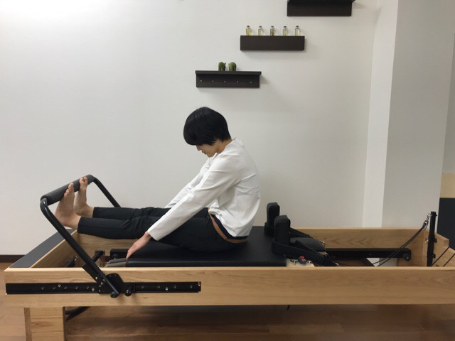 ピラティスリフォーマーでラウンドバックをする女性